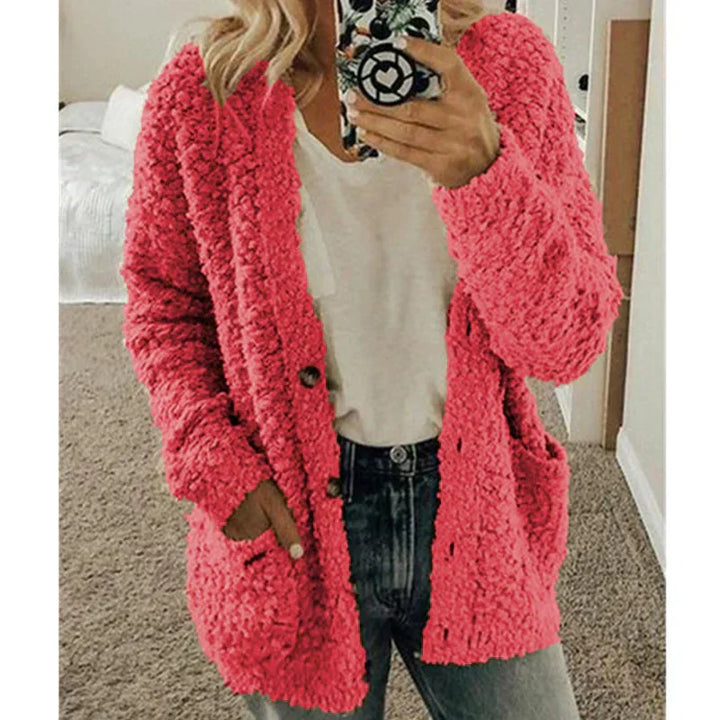 Frau in rosa Strickjacke, weißem T-Shirt und Jeans, hält Smartphone, gemütliche Mode.