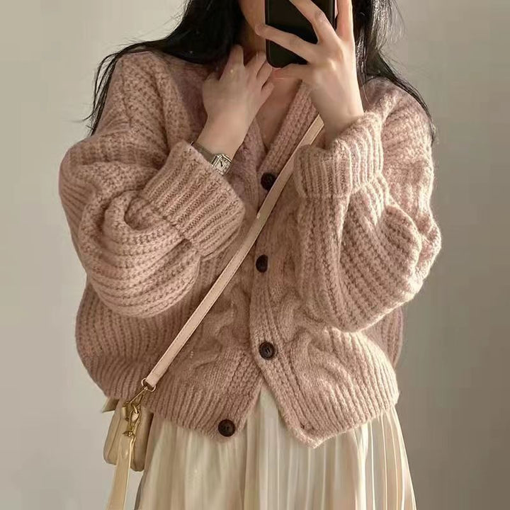 Frau trägt rosa Strickjacke mit Knöpfen, cremefarbenem Rock, Handtasche, Smartphone.