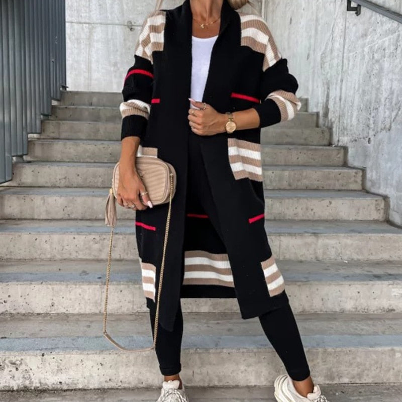 Frau in langem, gestreiftem Cardigan, schwarze Leggings, beige Tasche, weiße Sneakers.