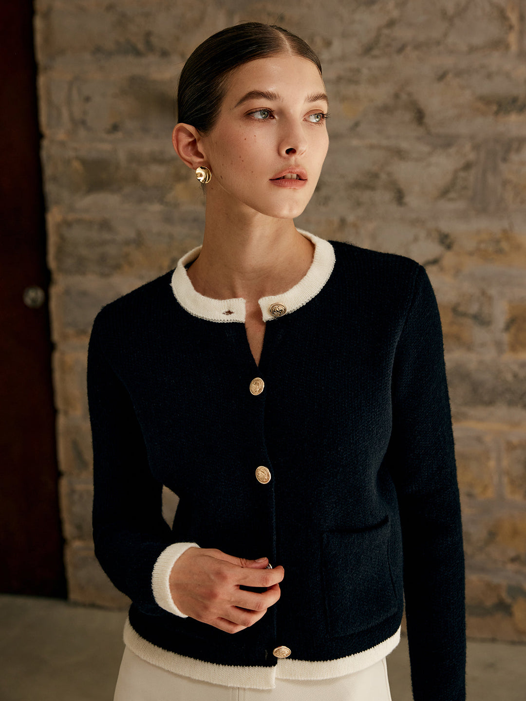 Frau in schwarzer Strickjacke mit weißen Details vor Steinwand, elegante Mode, Herbstkollektion.