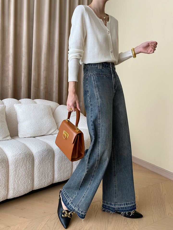 Frau in weißem Cardigan, blauer Jeans, brauner Handtasche, schwarzer Schuh; modisches Outfit.