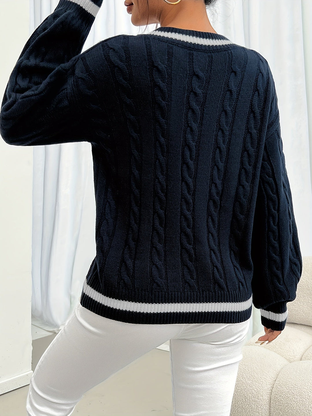 Frau in dunkelblauem Strickpullover mit Zopfmuster und weißen Akzenten, modisch, elegant.