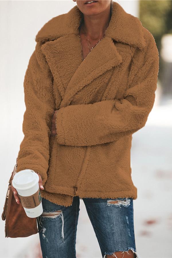 Frau in brauner Teddyjacke, hält Kaffeebecher, trägt zerrissene Jeans, Herbstmode.