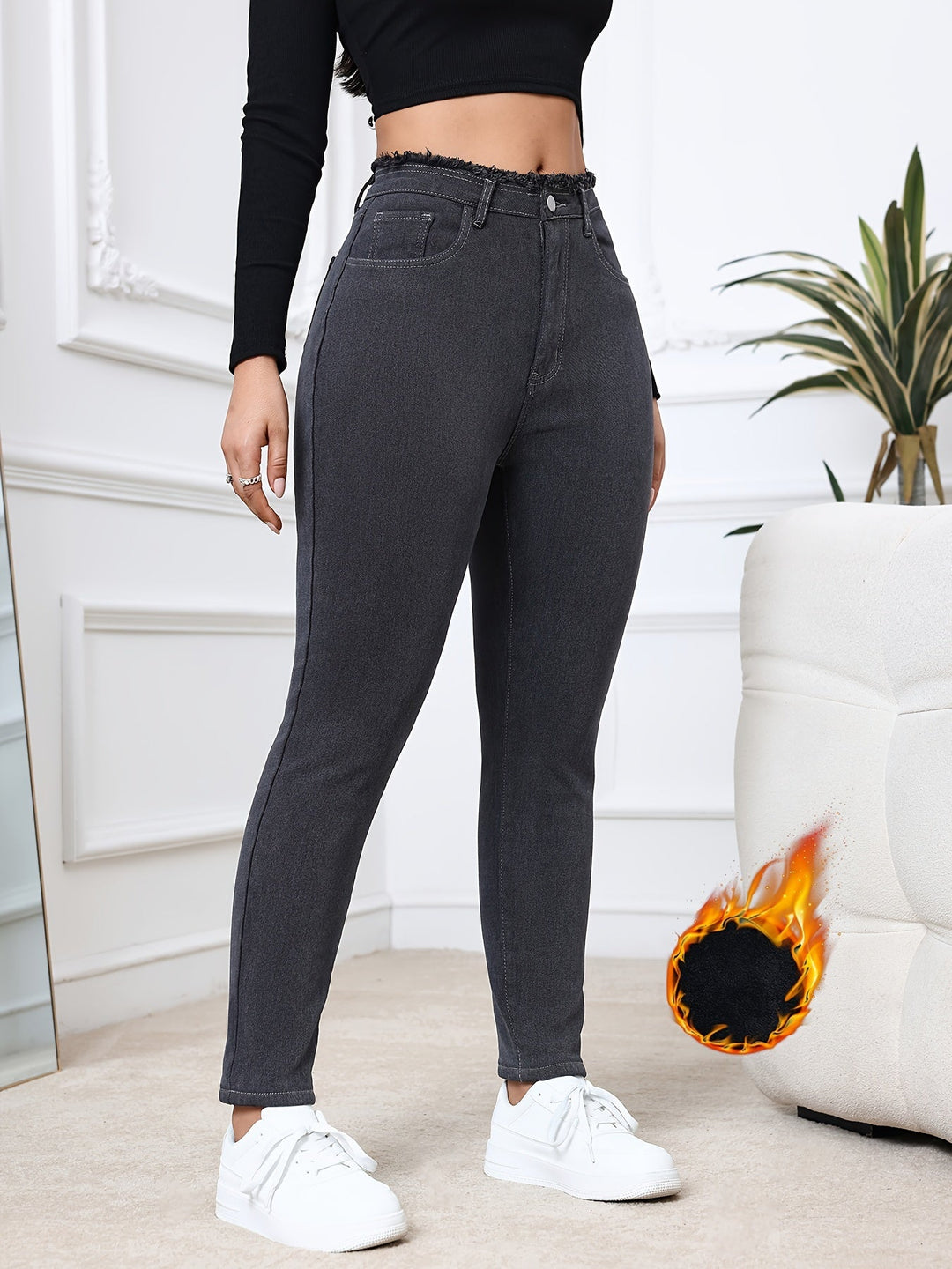 Frau in schwarzer Jeans und Crop-Top, weiße Sneaker, modernes Wohnzimmer, stilvolle Mode.