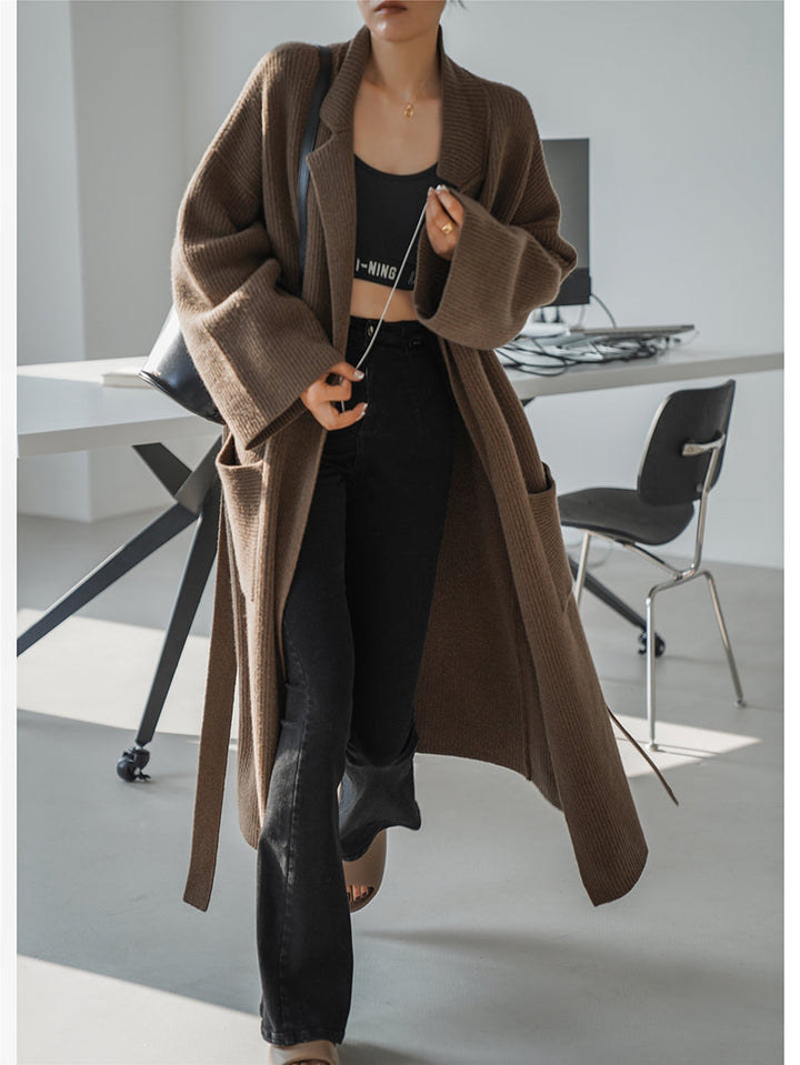 Frau im braunen Strickmantel, schwarze Hose, modernes Büro, Herbstmode, lässiger Stil.