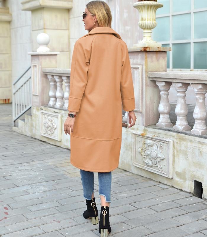 Frau in hellbraunem Ledermantel, Jeans und Stiefeletten auf gepflastertem Gehweg.