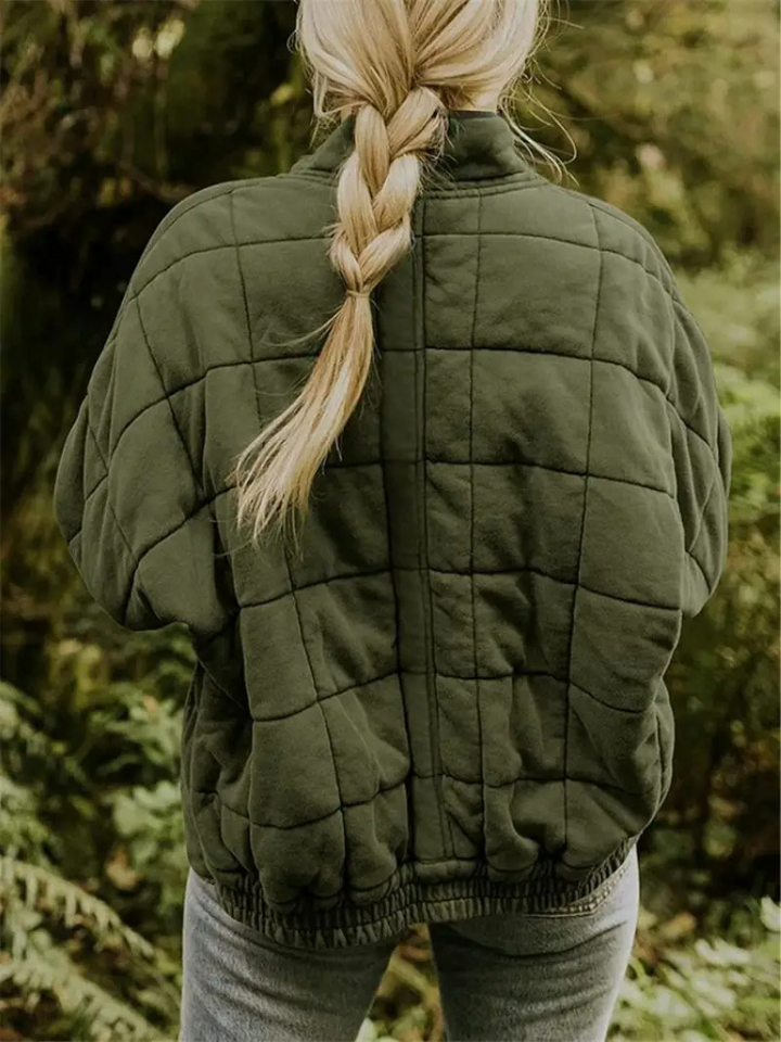 Frau in olivgrüner, gesteppter Übergangsjacke mit Zopf im Wald.