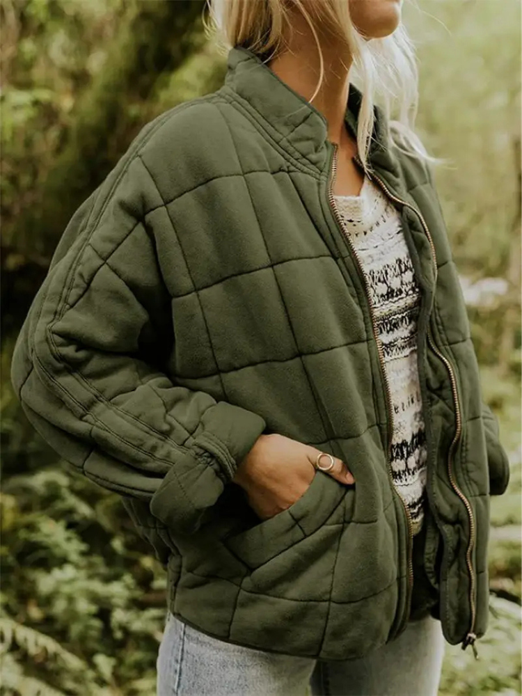 Frau in olivgrüner, gesteppter Übergangsjacke, oversized, mit Reißverschluss, im Freien.