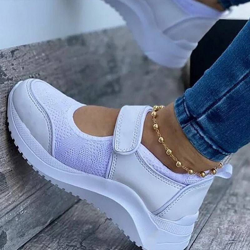 Weiße Damen-Sneaker mit Klettverschluss, atmungsaktiv, modisch, bequem, auf Holztreppe.