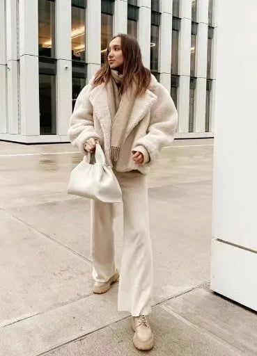 Frau in cremefarbener Teddyjacke und Hose, hält weiße Handtasche, moderne Wintermode.