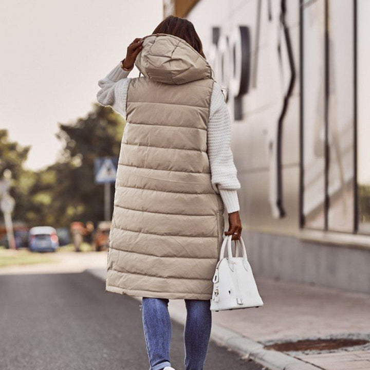Frau in beiger Steppweste mit Kapuze, weiße Handtasche, lässiger Herbstlook, Straße im Hintergrund.