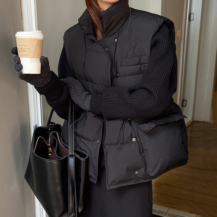Frau in schwarzer Steppweste mit Kaffeebecher und schwarzer Tasche, Wintermode, Indoor.