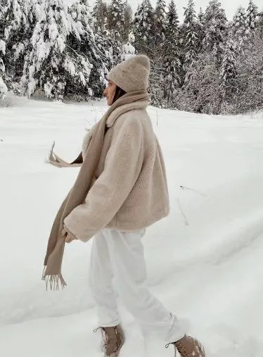 Frau im Winteroutfit mit beigem Mantel und Schal im verschneiten Wald spazieren.