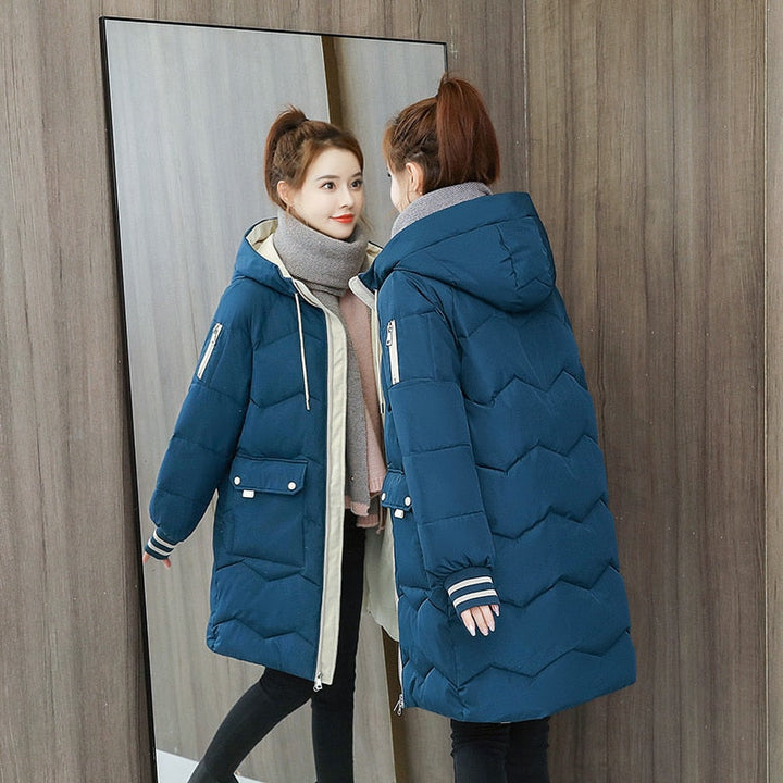 Frau in blauer Daunenjacke mit Kapuze, Wintermode, Spiegelbild, Holzvertäfelung, warmes Outfit.