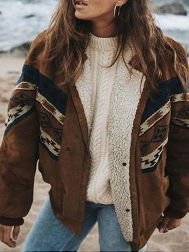 Frau in brauner Jacke mit Ethno-Muster und weißem Strickpullover am Strand.