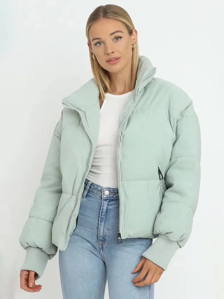 Frau in mintgrüner Daunenjacke, weiße Bluse, blaue Jeans, modisch, Winterkleidung.