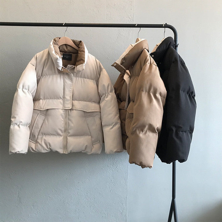 Drei Daunenjacken in Weiß, Beige und Schwarz auf Kleiderstange, Wintermode, warm, stilvoll.