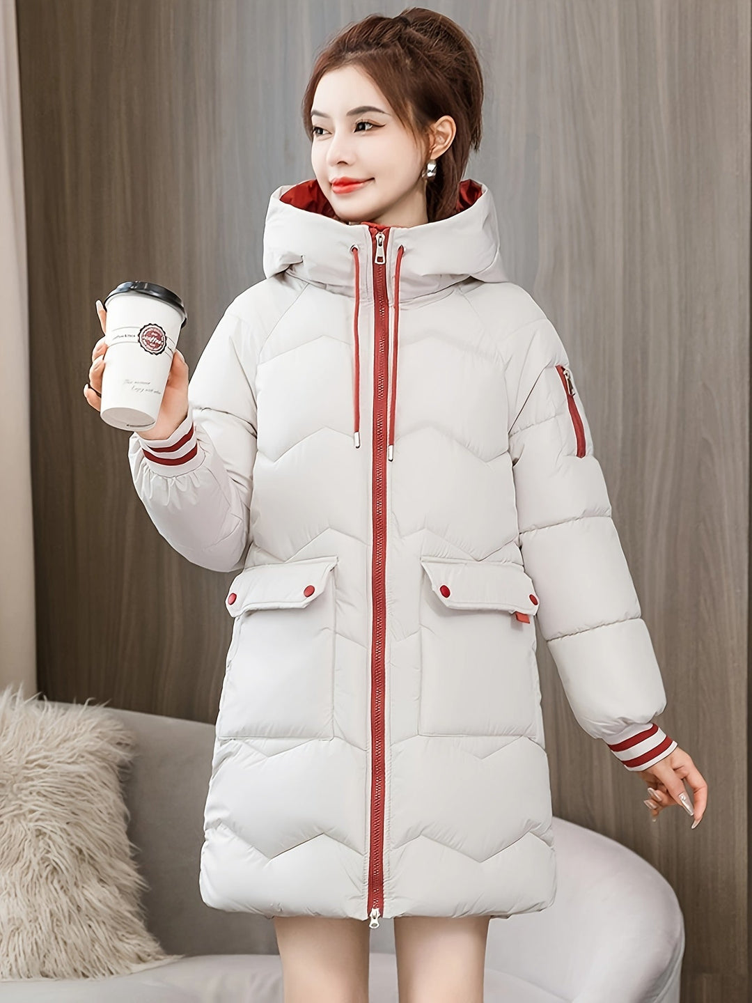 Frau in weißem Daunenmantel mit Kapuze hält Kaffeebecher, Wintermode, gemütlich, stilvoll.