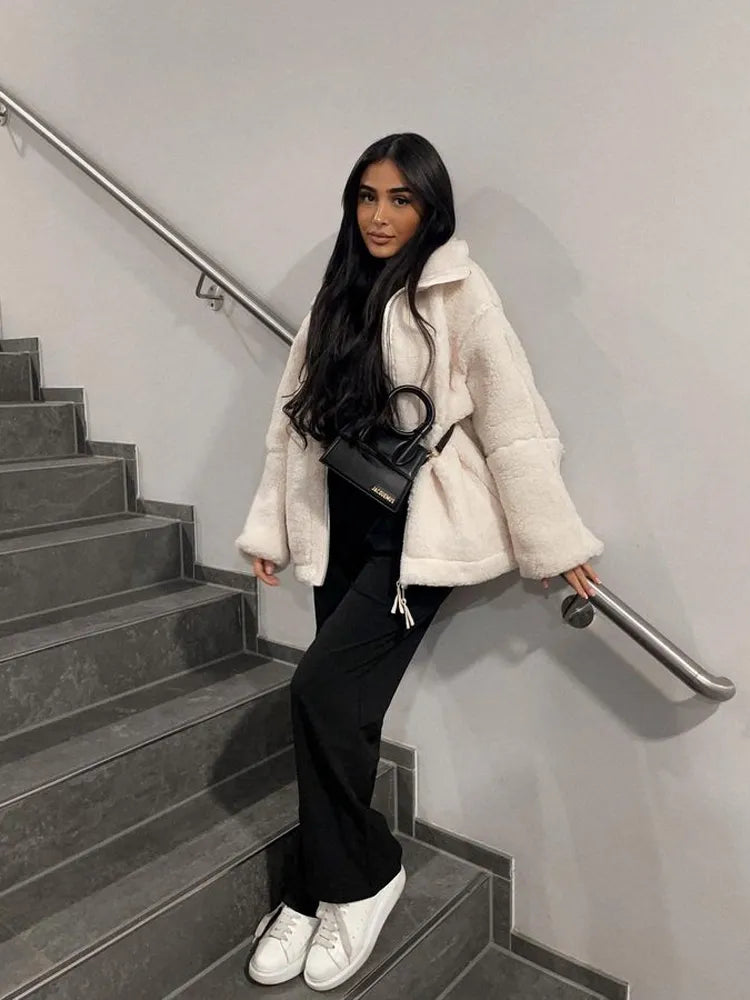Frau in weißem Kunstpelzmantel, schwarze Hose, weiße Sneaker, schwarze Umhängetasche auf Treppe.