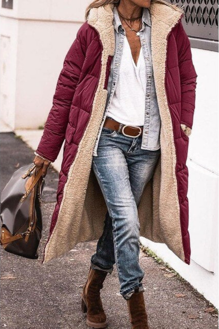 Frau in rotem Daunenmantel mit Fellfutter, Jeans und Stiefeln, modisch, winterlich, urban.