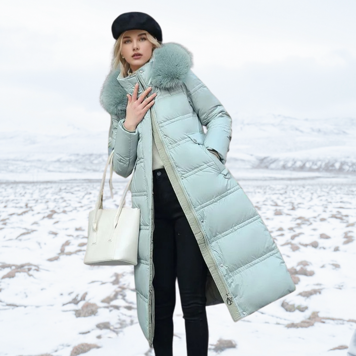 Frau in mintgrünem Daunenmantel mit Fellkragen, Wintermode, schneebedeckte Landschaft.