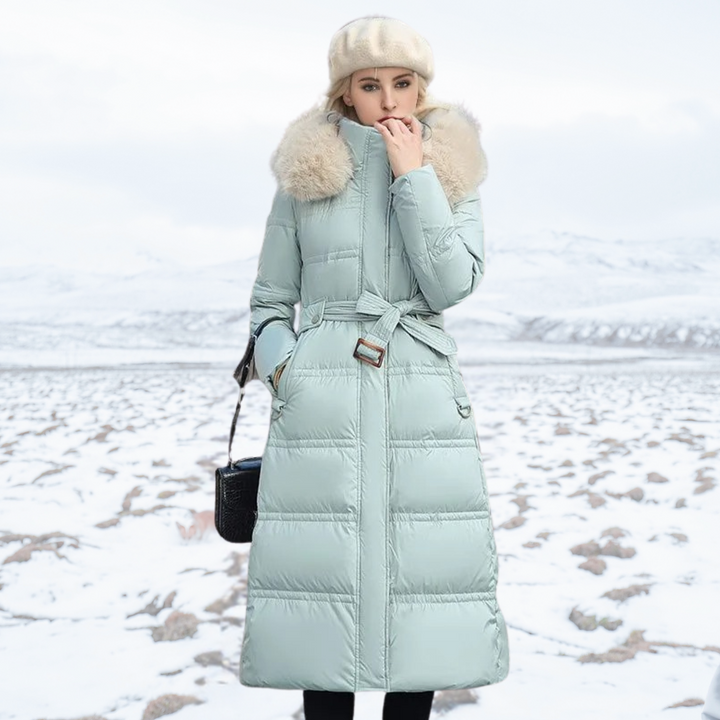 Frau in mintgrünem Daunenmantel mit Kapuze und Gürtel im verschneiten Winterlandschaft.