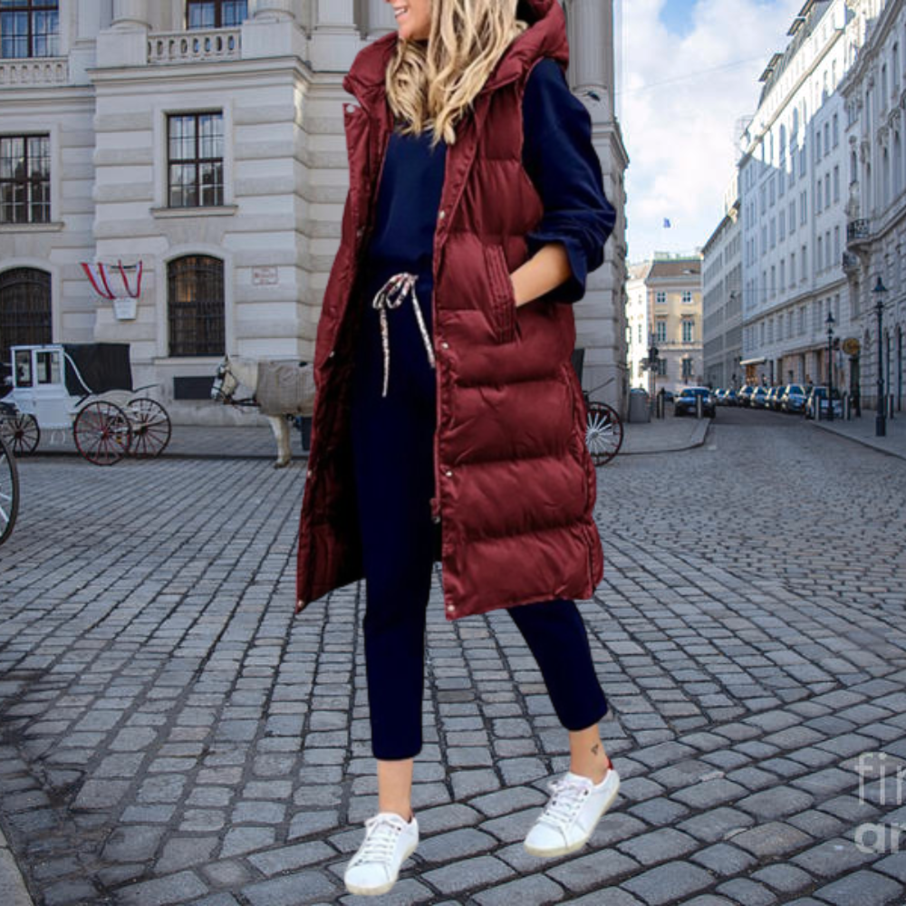 Frau in rotem Steppmantel, blauer Jogginghose und weißen Sneakers auf gepflasterter Straße.