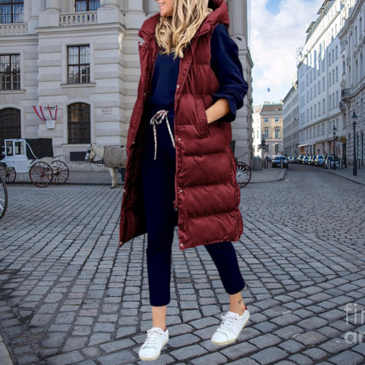 Frau in rotem Steppmantel, blauer Jogginghose und weißen Sneakers auf gepflasterter Straße.