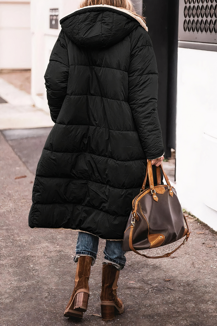 Frau in schwarzem Daunenmantel mit Kapuze, braune Lederstiefel, braune Ledertasche, Straße.