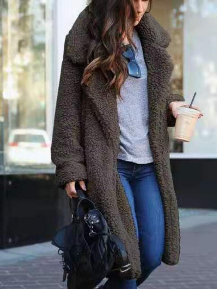 Frau in braunem Teddy-Mantel, grauem Shirt, blauer Jeans, mit schwarzer Tasche und Kaffee.