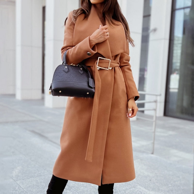 Frau in braunem Wollmantel mit Gürtel, schwarze Handtasche, städtische Kulisse.
