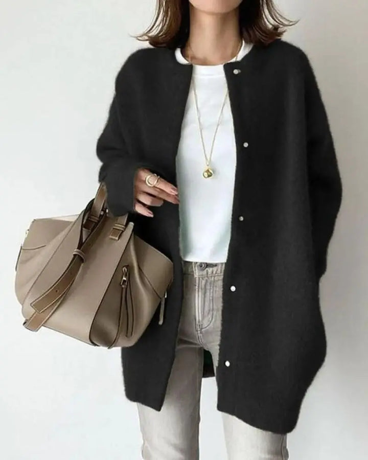Frau mit schwarzer Strickjacke, weißem T-Shirt, grauer Jeans und beiger Handtasche.