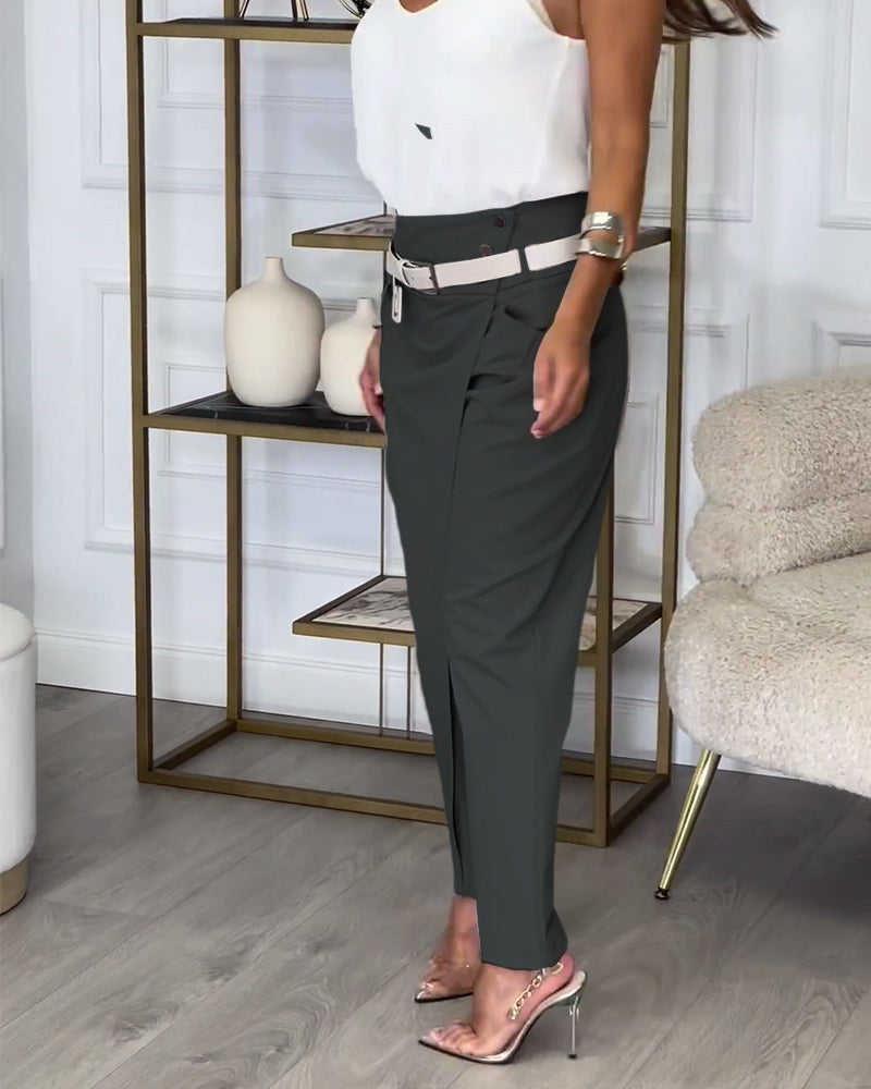 Frau in eleganter, dunkelgrauer Hose und weißem Top, steht in modernem Wohnzimmer.