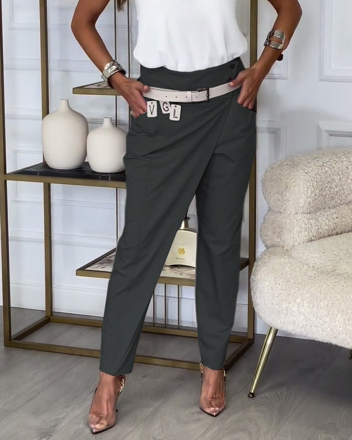 Frau in eleganter, dunkelgrauer Hose mit Gürtel, weißem Top, goldenen Schuhen, Wohnzimmer.