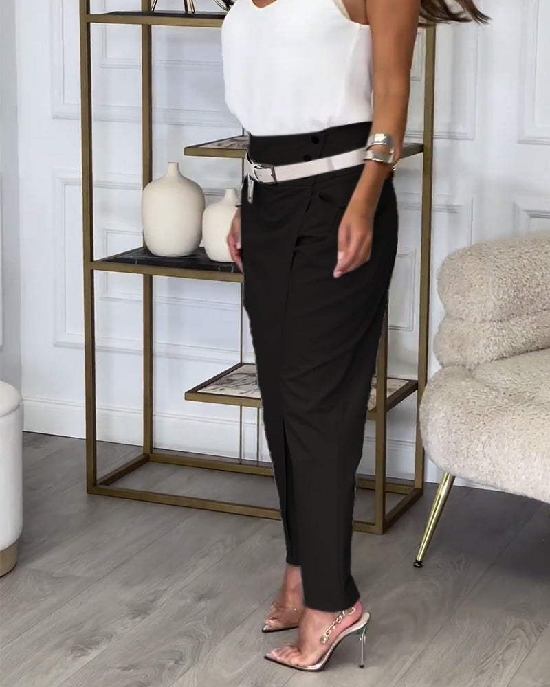 Frau in schwarzer Hose und weißem Top, steht in modernem Wohnzimmer, elegante Sandalen.
