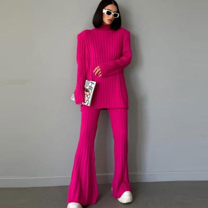 Frau in pinkem Strickanzug mit Schlaghose, hält Magazin, trägt weiße Sonnenbrille und Sneaker.