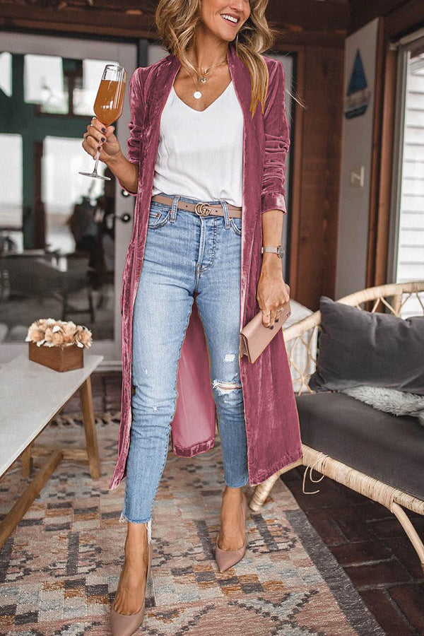 Frau in rosa Samt-Cardigan, weiße Bluse, zerrissene Jeans, hält Weinglas, modisch, elegant.