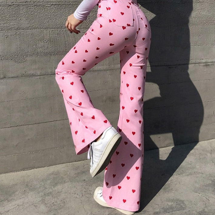 Frau in rosa Schlaghose mit roten Herzen, weiße Sneaker, modisch, trendige Damenmode.