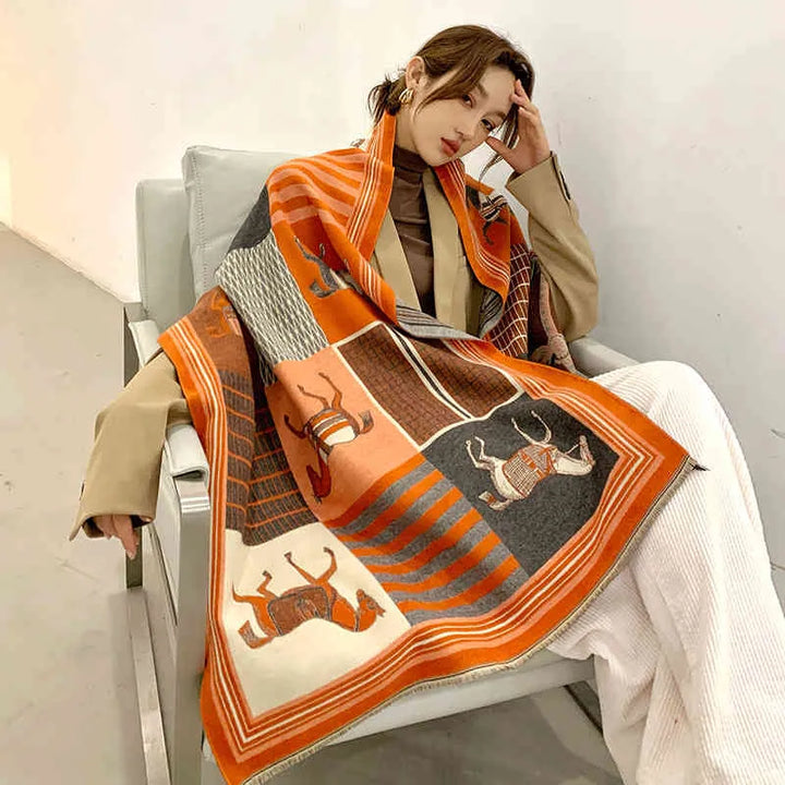 Frau mit orange-grauem Wollschal mit Tiermotiven, sitzt auf einem Sessel, modisch elegant.