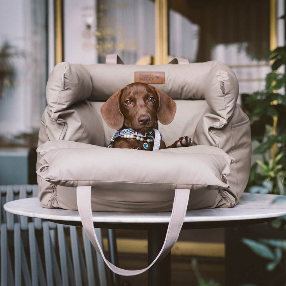 Brauner Hund in beigem Kunstleder-Autositz für Hunde auf Tisch, ideal für Reisen.