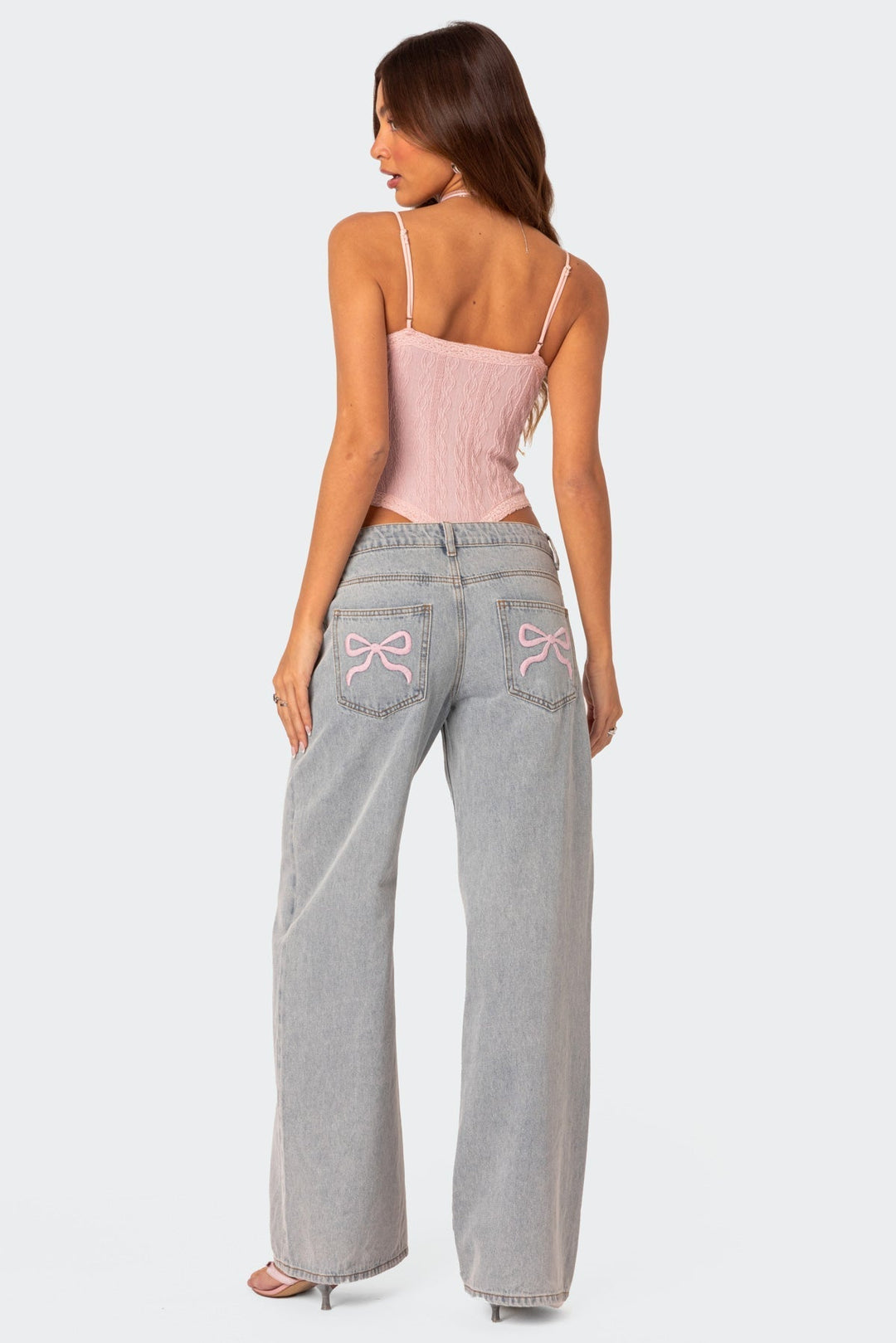 Frau in hellblauer Relaxed-Fit-Jeans mit rosa Stickerei, rosa Top, Rückansicht.