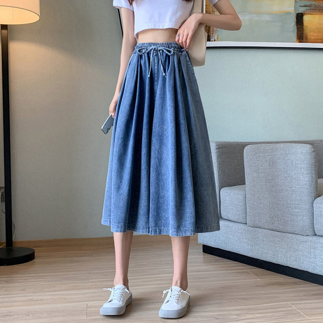 Frau trägt blauen Jeansrock, weißes Crop-Top, weiße Sneaker, modernes Outfit, Wohnzimmer.