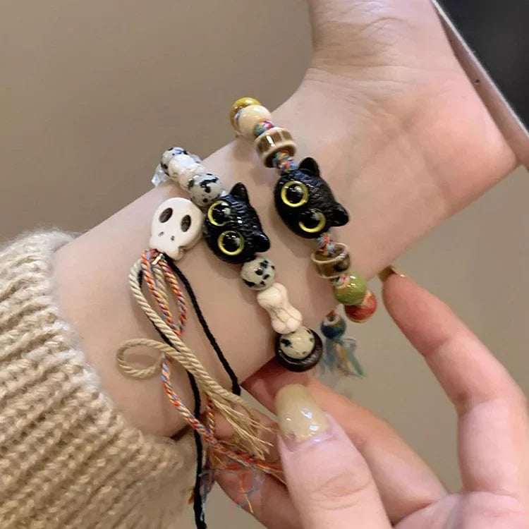 Armbänder mit schwarzen Katzenperlen, Totenkopf und bunten Details auf Handgelenk.