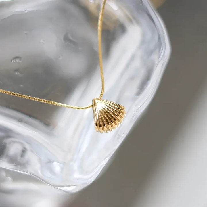 Goldene Muschel-Halskette auf Glas, elegantes Schmuckdesign, Damenaccessoire, Geschenkidee.