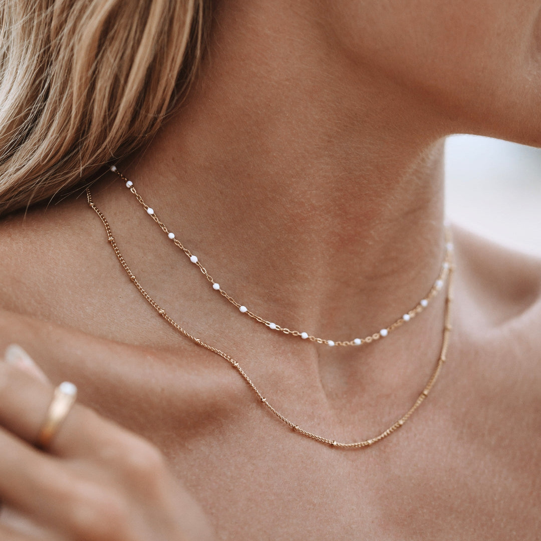 Frau trägt doppelte minimalistische Choker-Halskette aus Gold, eleganter Schmuck, Nahaufnahme.