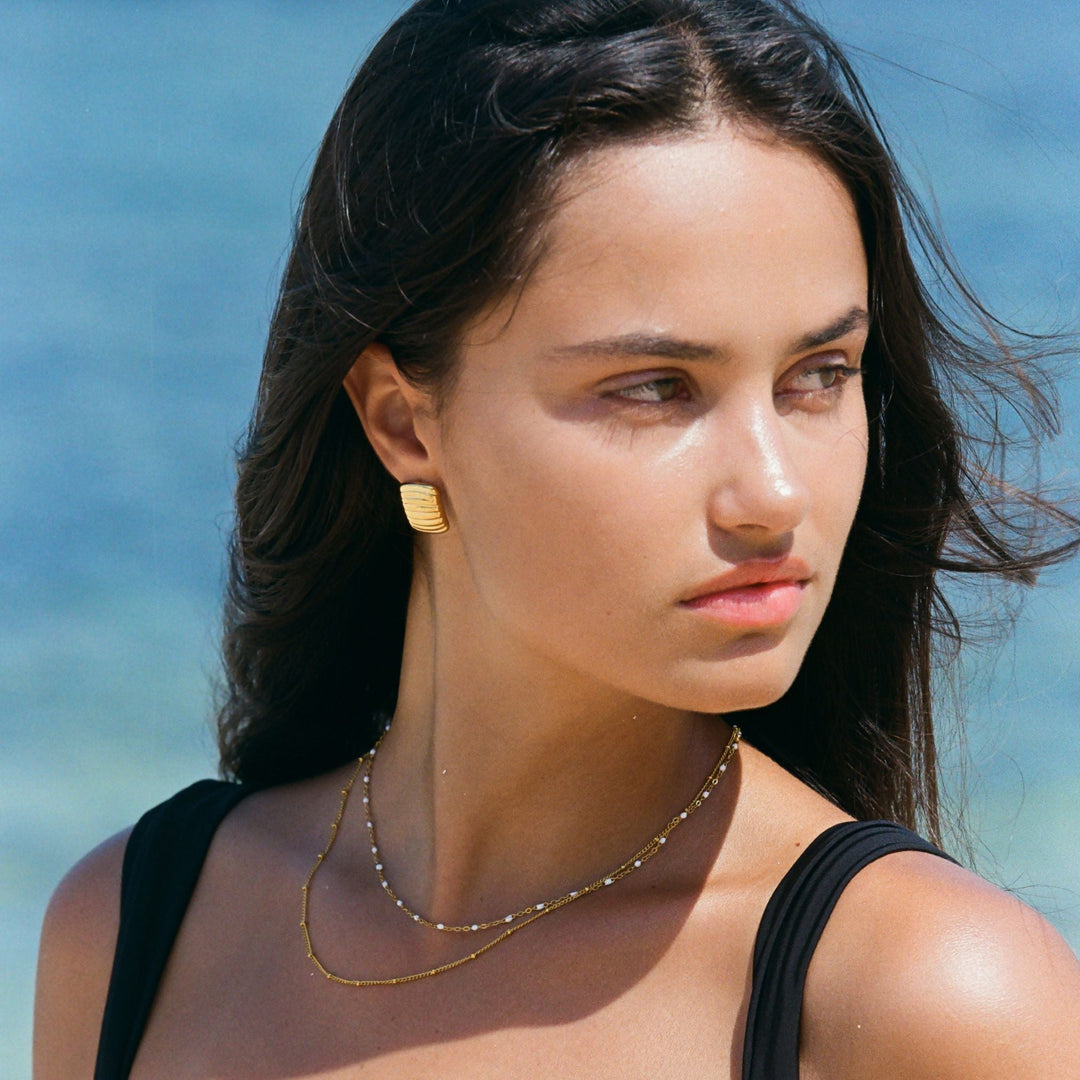 Frau mit zarter Doppelhalskette aus Gold am Strand, eleganter Schmuck, modisches Accessoire.