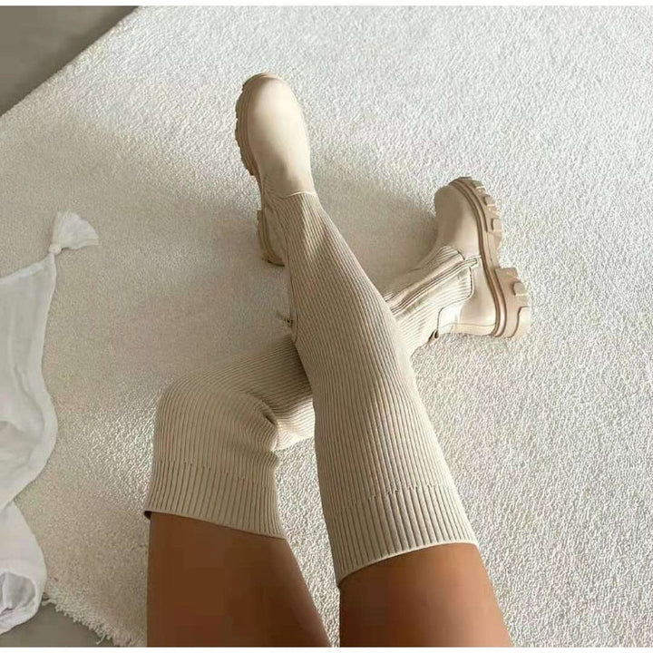 Beige kniehohe Stiefel mit gerippter Struktur auf weißem Teppich, modisch und elegant.