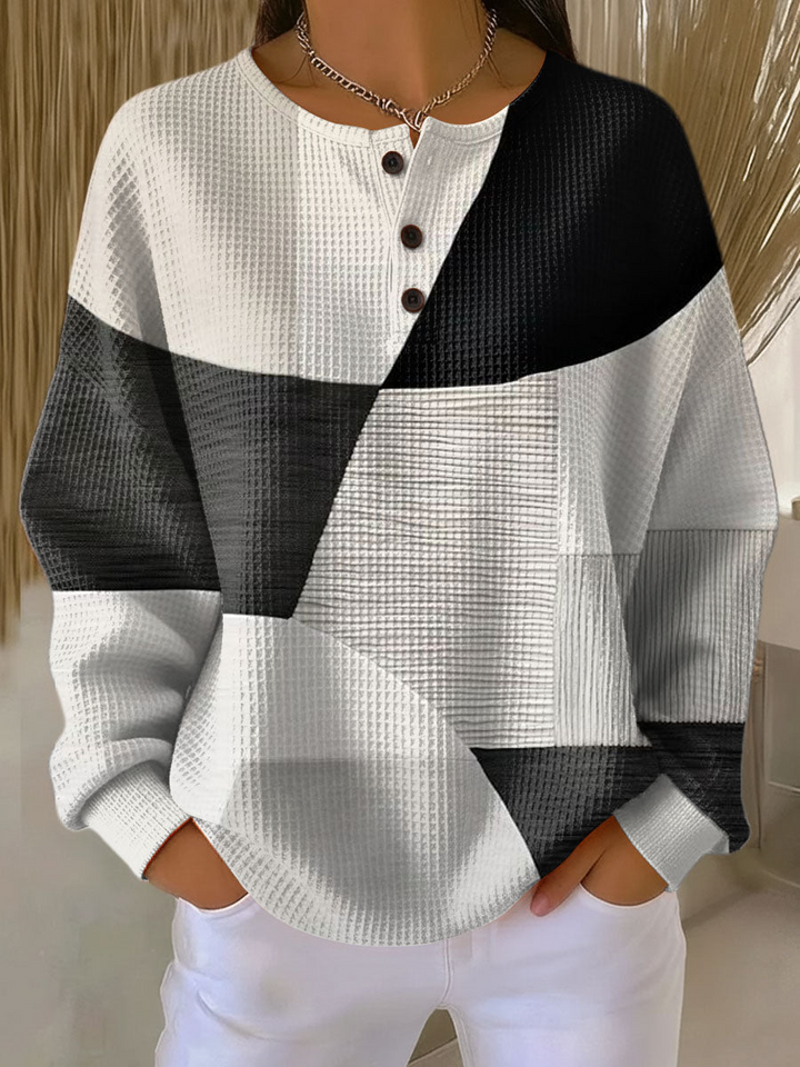 Vaflový svetr s knoflíky v černobílém geometrickém patchworku, pohled zepředu na modelce s rukama v kapsách. 2