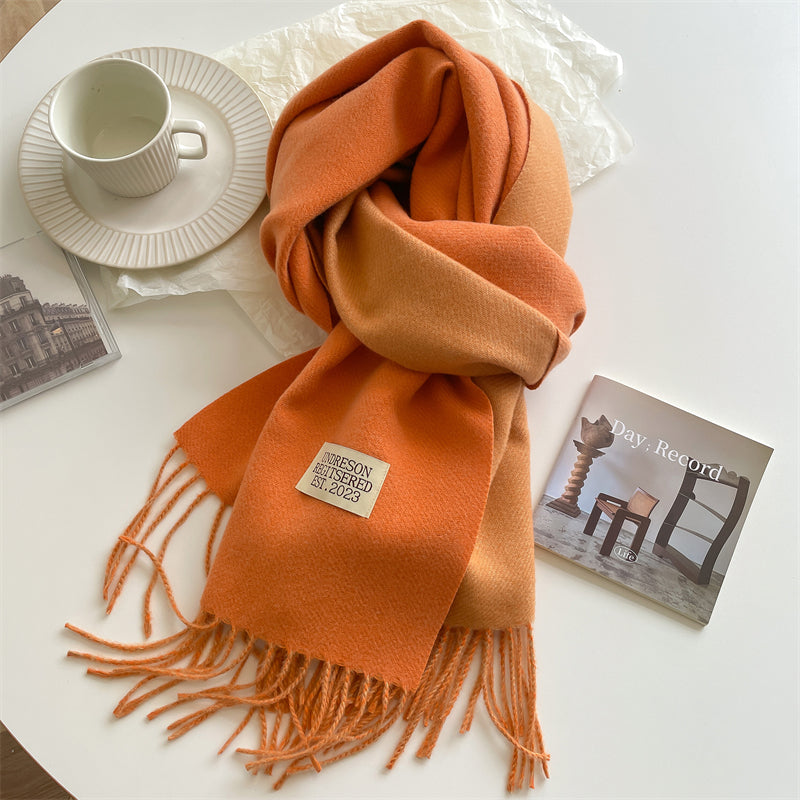 Orangefarbener Wollschal mit Fransen auf Tisch, neben Tasse und Magazin.