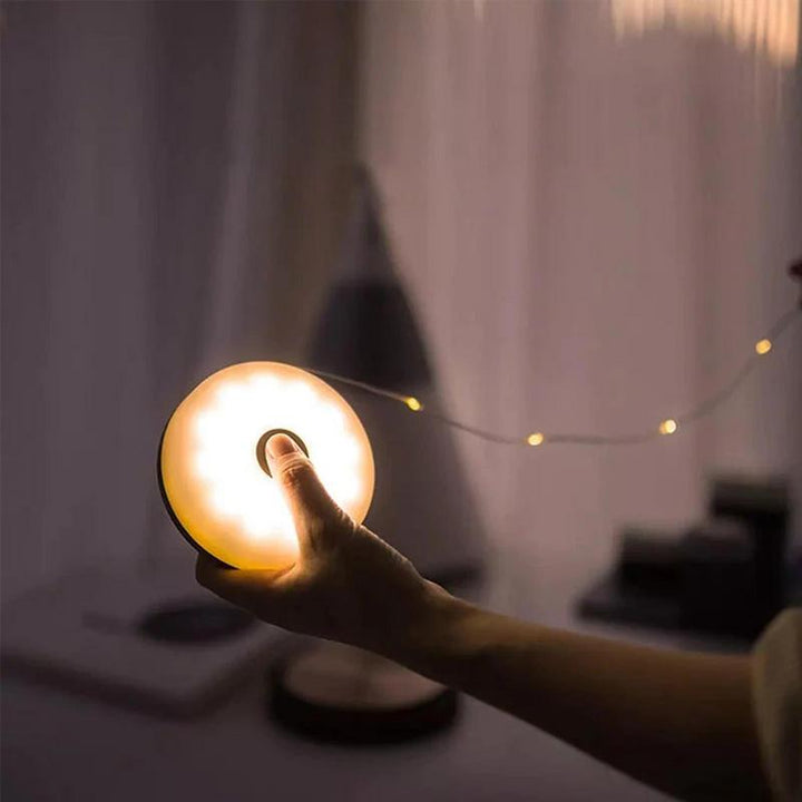 Hand hält runde LED-Lampe, warmweißes Licht, dimmbar, tragbar, modernes Design, Innenbeleuchtung.